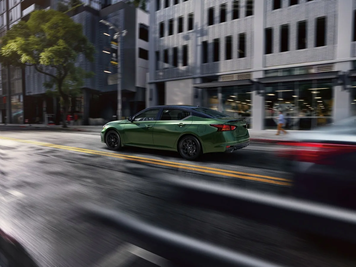 Nissan Altima in green driving through a city street, side view